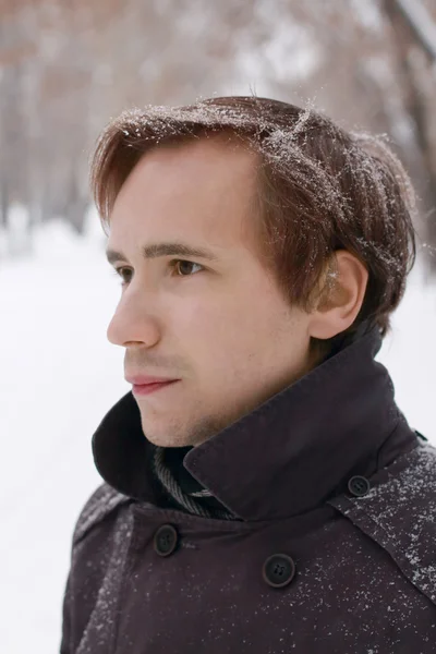 Young man with snowflakes in hair looks at distance outdoor at w — Stock Photo, Image