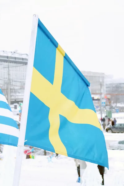 Flag of Sweden on wind at winter cloudy day in street of city — Stock Photo, Image