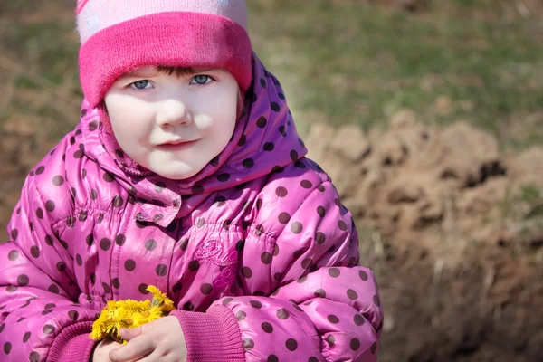 Pequena menina bonita segura flores amarelas e olha na câmera — Fotografia de Stock