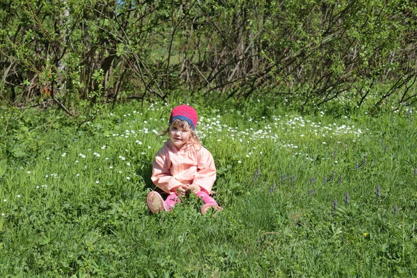 Счастливая маленькая девочка в розовом сидит на зеленой траве весной — стоковое фото
