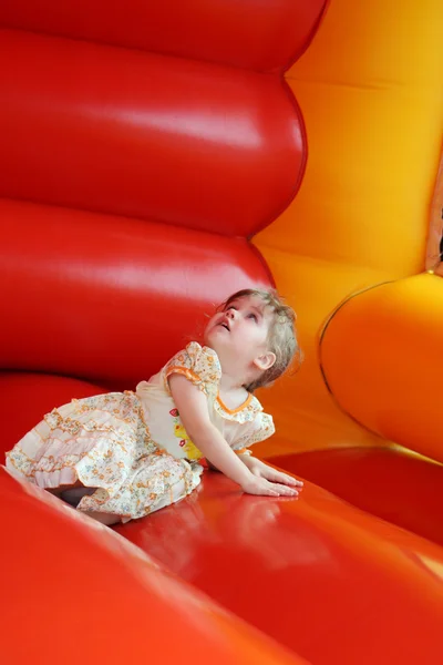 Pequena menina feliz bonita jaz no castelo bouncy vermelho e olha — Fotografia de Stock