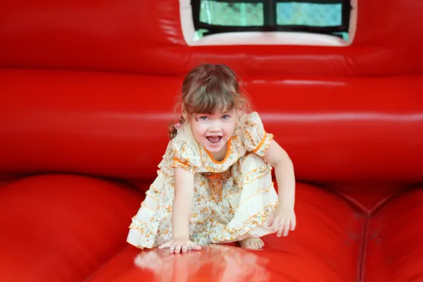 Little beautiful girl in dress plays in red bouncy castle and sh — Stock Photo, Image