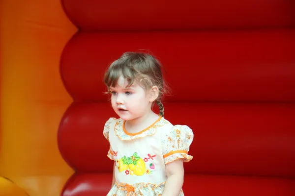 Little beautiful happy girl jumps on red bouncy castle and looks — Stock Photo, Image