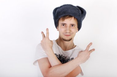 Happy young man in grey cap with earflaps shows two gesture peac clipart