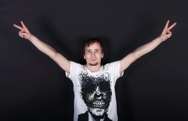 Щасливий молодий чоловік у білій сорочці показує два жести мир на чорному — стокове фото