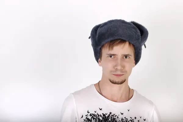 Young man in grey cap with earflaps looks surprised in studio — Stock Photo, Image