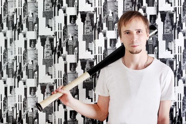 Jonge ernstige man met baard in shirt staat met bat in de buurt van muur — Stockfoto