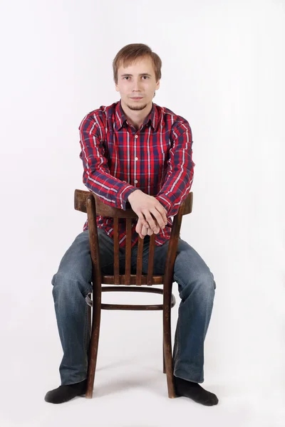 Young man with beard in checkered red shirt sits astride chair — Stock Photo, Image