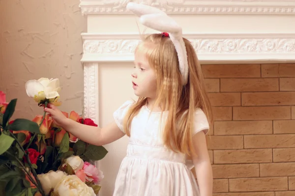 Little beautiful girl in white dress and bunny ears pulls out wh — Stock Photo, Image