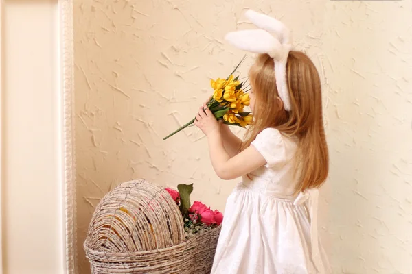 Маленькая красивая девочка в белом платье и кроличьи уши нюхают поплавок — стоковое фото