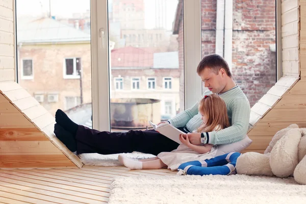 Küçük sarışın kız ve babası pencere oturup bo okuyun — Stok fotoğraf
