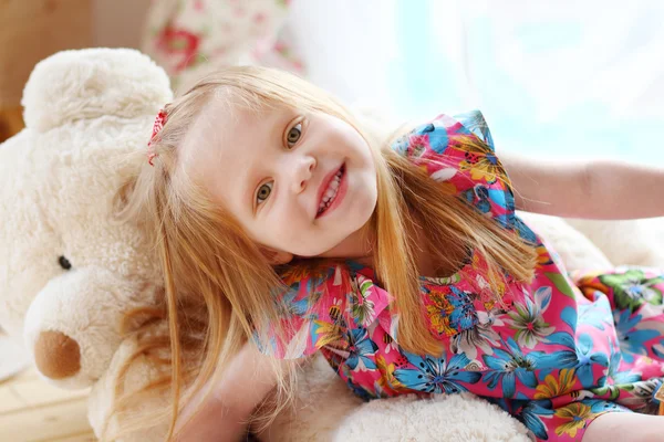 Bonita niña rubia se encuentra en el gran oso de juguete suave y sonríe —  Fotos de Stock