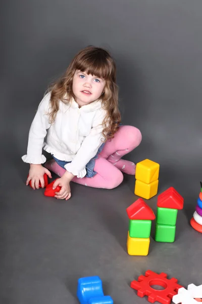 Little girl sitting on floor and builds tower of blocks — Stock Photo, Image