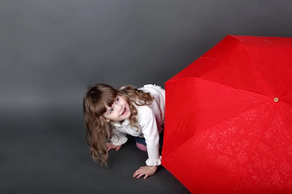 Little girl playing peeking from behind large red umbrella — Stock Photo, Image