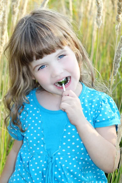 Menina em vestido azul com doces na boca na grama alta — Fotografia de Stock