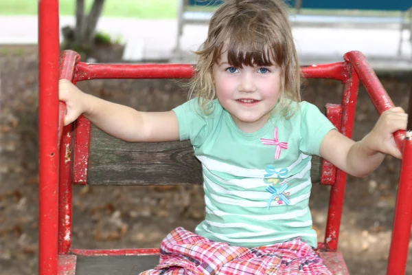 Joyful little girl plays on red swing — Stock Photo, Image