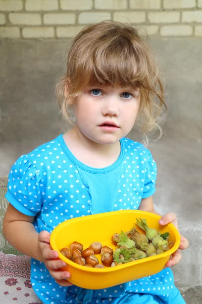 Маленькая девочка в синем платье держит миску с лесными орехами — стоковое фото