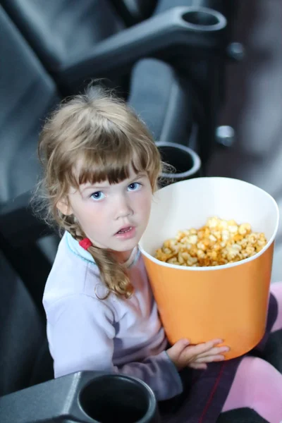 大份爆米花坐在电影院大厅的小女孩 — 图库照片
