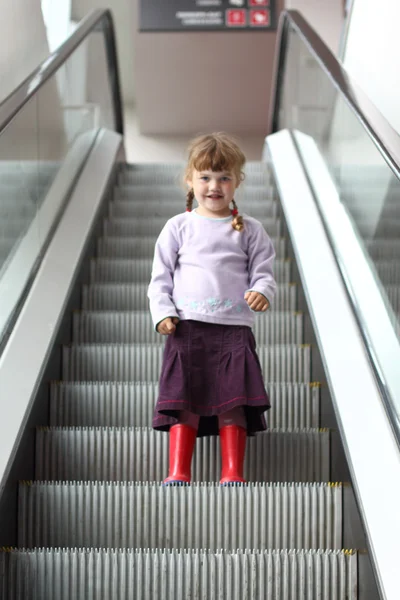 Kleines Mädchen mit Zöpfen und Gummistiefeln kommt Rolltreppe hinunter — Stockfoto