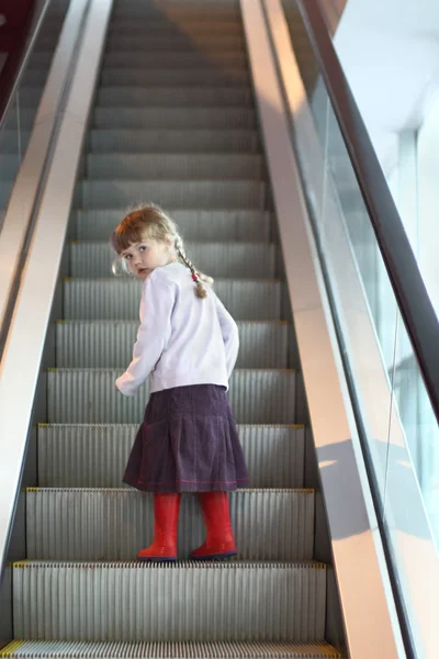 Little girl with pigtails and gumboots looks back on escalator — Stock Photo, Image