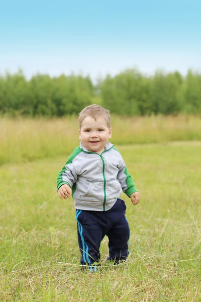 Knappe lachende jongetje staat op groene weide in zomerdag — Stockfoto