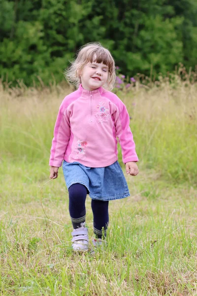 Pequena menina bonita na saia indo e martelando no prado verde — Fotografia de Stock