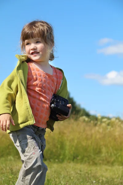 Ładna dziewczynka posiada aparat fotograficzny i patrzy daleko na łące w podsum — Zdjęcie stockowe