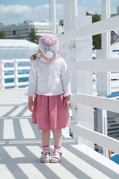 Pequena menina bonito fica na ponte de madeira branca e olha para baixo — Fotografia de Stock