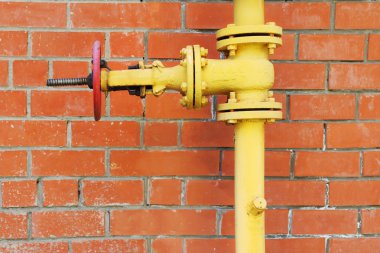 Sarı metal gaz boru hattı ile kırmızı tuğla arka plan üzerinde Vana 