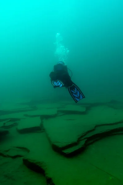 Mergulhador SCUBA nadando sobre grandes placas de rocha — Fotografia de Stock