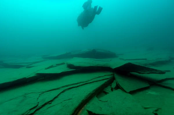 Buceador SCUBA nadando sobre grandes placas de roca —  Fotos de Stock