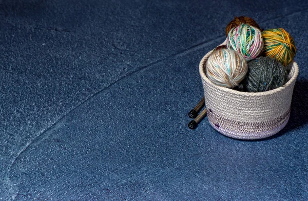 Espetos de agulhas de tricô de fios em uma tigela de tecido bege e fundo azul — Fotografia de Stock