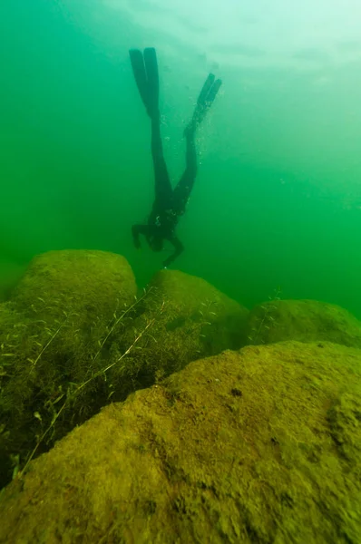SCUBA subacqueo esplorare un lago interno nuvoloso con grandi massi — Foto Stock
