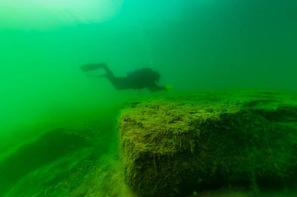 SCUBA subacqueo esplorare un lago interno nuvoloso con grandi massi — Foto Stock