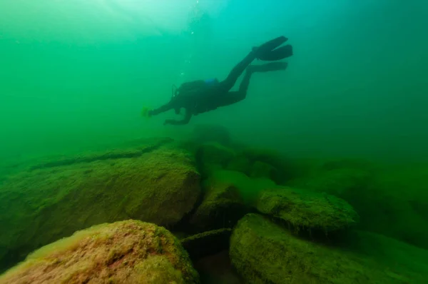 SCUBA potápěč zkoumající zamračené vnitrozemské jezero s velkými balvany — Stock fotografie