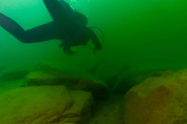SCUBA subacqueo esplorare un lago interno nuvoloso e massi con una torcia subacquea — Foto Stock
