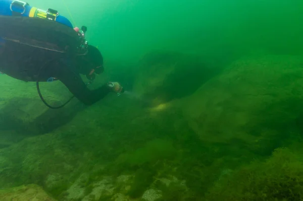 SCUBA potápěč zkoumající zamračené vnitrozemské jezero a balvany s potápěčskou pochodní — Stock fotografie