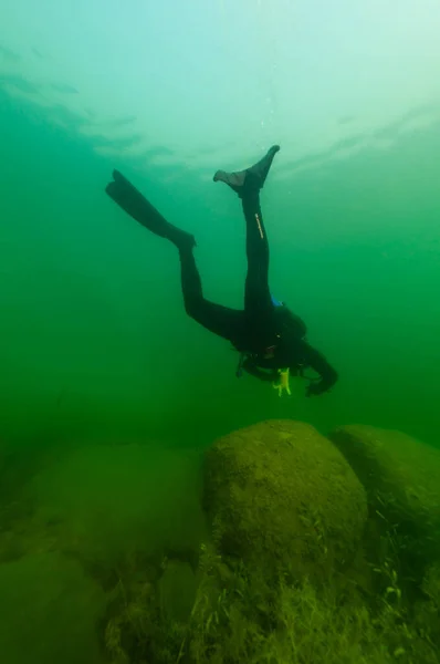 SCUBA diver exploring a murky inland lake with large boulders — Foto Stock