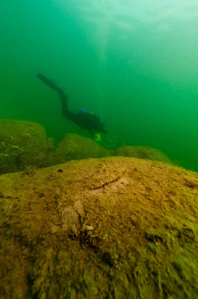 Mergulhador SCUBA explorando um lago interior escuro com grandes rochas — Fotografia de Stock