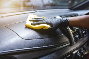 Eldivenli teknisyen kırmızı bezle arabanın ön panelini temizliyor. Konulu araba yıkama ve bakım.