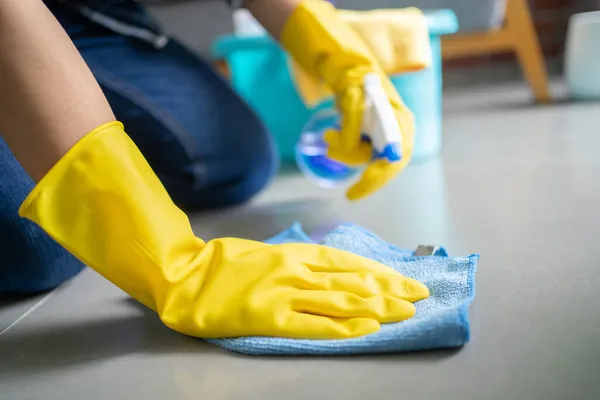 Cleaning concept, Happy young woman in blue rubber gloves wiping dust using a spray and a duster while cleaning on floor at home.