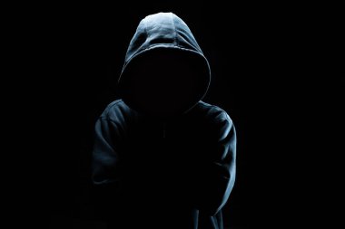 Siyah maskeli ve kapüşonlu bilgisayar korsanı. Karanlık bir yüz. Veri hırsızlığı, internet dolandırıcılığı, siber güvenlik kavramı.