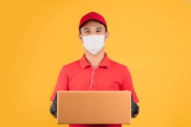 Teslimatçı adam kırmızı bir şapka ve üniforma içinde bir tişört giyer. Maske takıyordu, eldivenleri boş bir karton kutu tutuyordu..