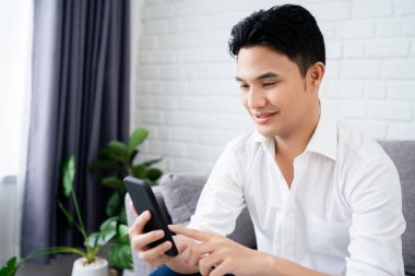 Evdeki koltukta oturan rahat adam akıllı telefon kullanıyor..