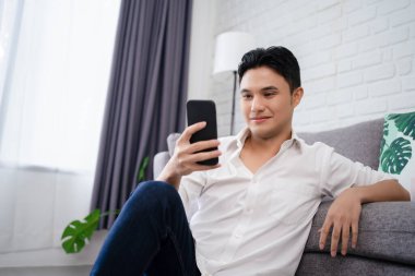 Çekici zeki genç adam oturma odasında yerde oturuyor, cep telefonu kullanıyor.