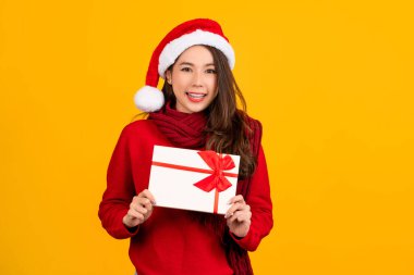 Noel Baba 'nın kırmızı arka plan stüdyo resminde izole edilmiş hediye sertifikasına Noel şapkası işaret parmağı takan genç bir kadın. Mutlu yıllar, mutlu noeller.