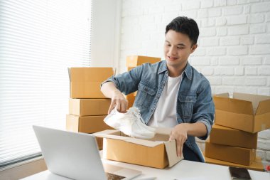 Küçük işletme KOBİ 'si, yakışıklı Asyalı adam ürünü bir paket kutuda hazırlıyor. Çevrimiçi fikirler satılıyor.