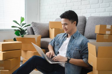 Çevrimiçi alışveriş yapan Asyalı genç adam iş yerinde karton bir kutuda küçük bir iş kuruyor. Satıcı, müşteri, çevrimiçi satış veya ekommerce için dağıtım kutusunu hazırlar..