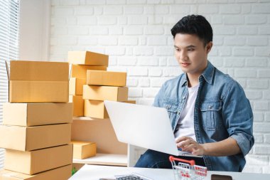 Asyalı işyeri sahibi kutu paketlerini hazırlamak için çevrimiçi siparişleri kontrol etmek için bir tablet kullanıyor. Çevrimiçi satış kavramı.