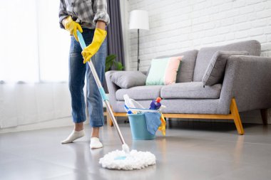 Temizlik çubuğu tutan genç bir kızın kesilmiş görüntüsü oturma odasını paspaslıyor.